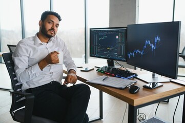 Thoughtful concentrated indian business man entrepreneur investor manager using computer, watching webinar working in office analyzing online data market thinking doing web research looking at laptop.