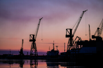 Port cranes at sunset. Port, cargo transportation and cargo ships. Selective focus