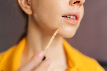 Detail close-up of unrecognizable young woman with natural beauty applying foundation on face to correct skin and hide pimples near lips. Female doing makeup putting base tone cream using concealer.