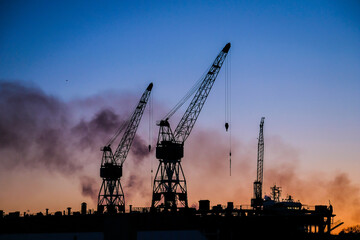 Port cranes at sunset. Port, cargo transportation and cargo ships. Selective focus