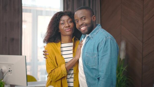 Portrait of happy African American couple smiling at camera. Handsome man and beautiful wife standing near computer. Attractive young family feeling good together. Relationship concept.