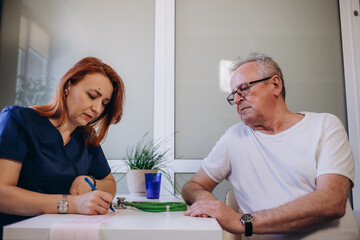 Female professional doctor showing medical test result explaining prescription using digital tablet app visiting senior man patient at home sitting on sofa. Elderly people healthcare tech concept.