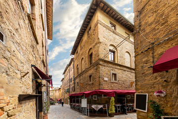A small corner and sidewalk cafe in a narrow alley with high stone walls in the medieval center of the hilltop village of Volterra, Italy, in the Tuscany region.