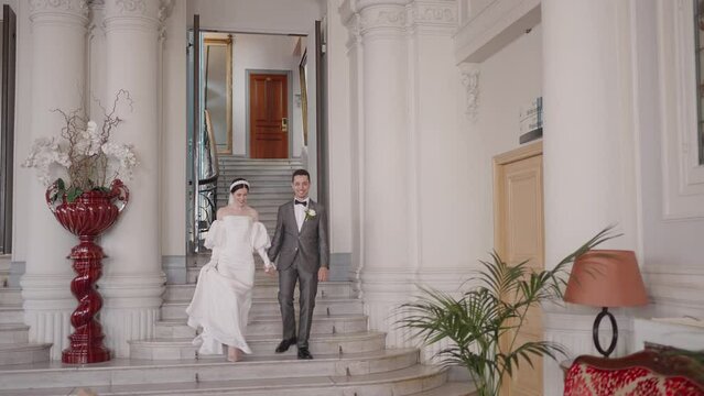 Man and bride go down stairs. Action. Newlyweds in outfits descend from registry office. Bride and groom go down stairs of registry office