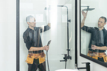 The worker is connecting the glass walls of the shower enclosure with a metal bar.