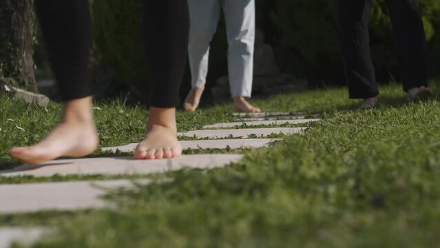A group of people are walking barefoot along a path made of tiles and grass. Meditation in the framework of the Mindfulness program
