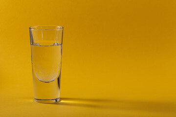 Glass of pure sparkling water on yellow background with trendy shadows and reflections. Free space for text