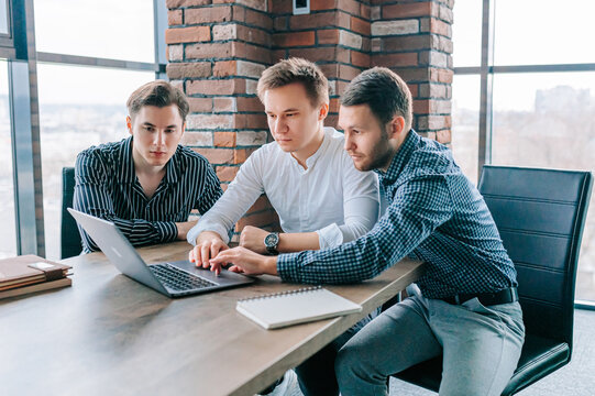 A male mentor providing one-on-one training to a trainee on a laptop in a corporate environment. Three colleagues deep in concentration, typing away on their laptops while their mentor provides