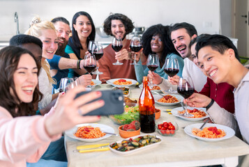 group of multiethnic friends take a smartphone selfie while eating pasta and toasting with wine