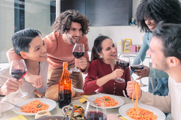 Multiethnic friends eating pasta and drinking wine at home