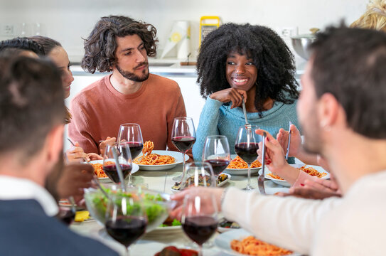 Multiethnic  friends eat spaghetti with tomato sauce together in the kitchen of a shared apartment