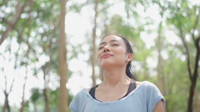 young Asian woman person breath a nature fresh air, relax and freedom lifestyle to happy in green park beautiful girl at summer travel and enjoy vacation with a tree outside for health careful