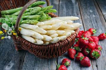 Reife rote Erdbeeren und Spargel aus biologischem Anbau angeboten als close-up in einem Korb auf einem rustikalen alten Holz Board