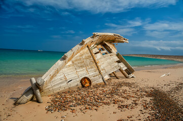 a broken boat thrown out on a deserted beach on the ocean.