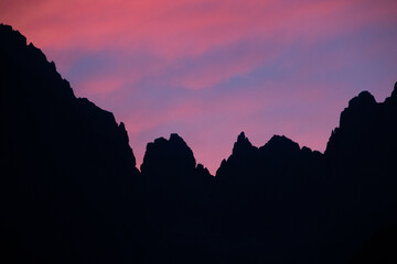 Fototapeta premium Rugged peaks of the mountain range are silhouetted against a stunning sunset sky, awash with a kaleidoscope of warm and pink colors that create a truly breathtaking vista. Dolomites, Alps, Italy.