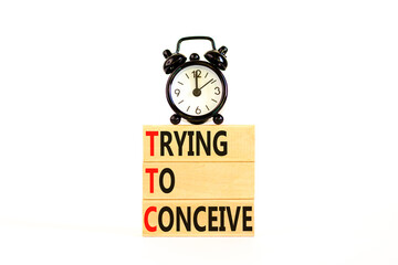 TTC trying to conceive symbol. Concept words TTC trying to conceive on wooden blocks on beautiful white table white background. Black alarm clock. Medical TTC trying to conceive concept. Copy space.