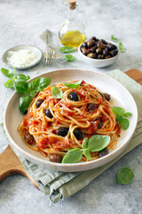 Pasta with tomato sauce, dark olive and parmesan cheese on light background. Spaghetti alla puttanesca. Top view.