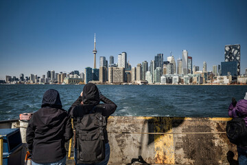 two tourists taking a picture from ferry in lake ontario of toronto skyline