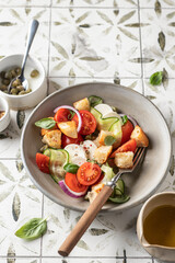 Fototapeta na wymiar Traditional italian tomato salad panzanella with mozzarella, capers, red onion, croutons, cucumbers and basil. Summer salad on printed tile background with copy space