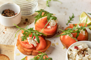 Bruschetta with tomatoes, arugula, olive oil and cheese on white tray on textured background. Fresh italian toasts