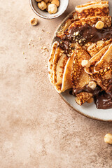 Crepes with chocolate and hazelnuts on beige background. Thin pancakes as delisious breakfast or dessert concept, Pancake day, Maslenitsa. Copy space