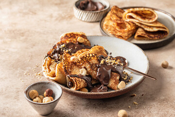 Crepes with chocolate and hazelnuts on beige background. Thin pancakes as delisious breakfast or dessert concept, Pancake day, Maslenitsa