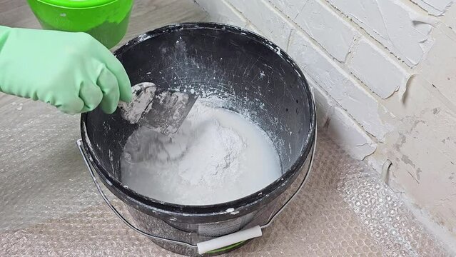 The hand of the master stir the plaster in a bucket with a spatula