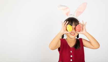 Happy Easter Day. Smile Asian little girl wearing easter bunny ears holding colorfull eggs closes eyes with testicles isolated on white background with copy space, Happy child in holiday