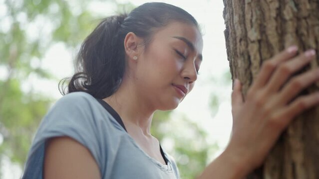 Environment Earth Day and Sustainable green energy concept, Asian female give a love to nature care connecting hands to hugging and touch a tree in forest, woman relaxation with ecology protection