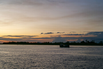 Sunset over the Amazon river with a riverboat in the foreground and dark silhouette of trees and clouds