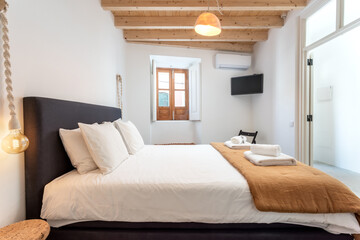 Traditional modern Iberian bedroom with wooden ceiling and clean towels and linens.