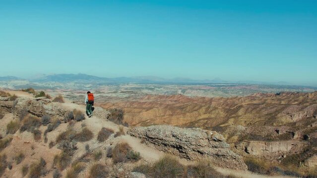 Outdoor lifestyle of a male traveler takes him to the top of a desert hill, where he gazes in awe at the majestic mountains. The scenic views inspire his sense of wanderlust and adventure. 