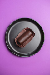 Close-up chocolate candies on a black plate and purple background. View from above.