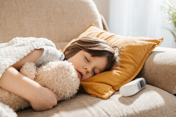 A little boy feels unwell, gets sick and lies on the sofa in the living room, resting in an embrace with his favorite toy. Period of influenza and viral diseases