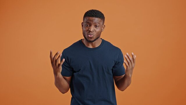 Confused dark-skinned guy asking what, looking astonished at camera, isolated on orange background