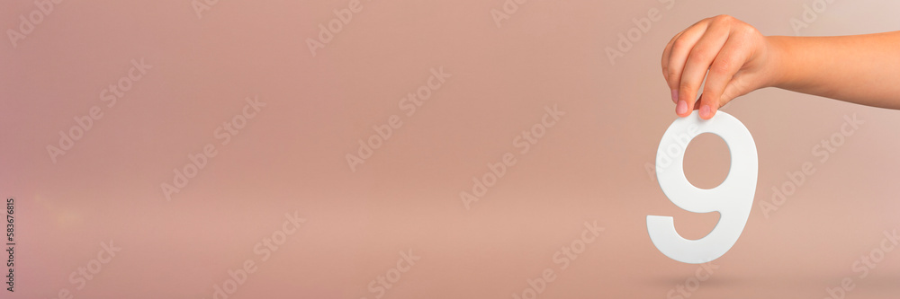 Aufkleber number nine in hand. a hand holds a white number 9 on a red background. concept with number nine. bi