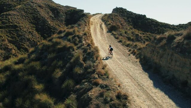Professional athlete suffers and takes on challenge of cycling gravel bike uphill in desert scenic beauty. Peaceful view of mountains inspires sportsman sense of adventure and wanderlust. 