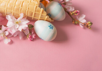 easter eggs and cherry flowers on a pink background with bokeh and copy space.
