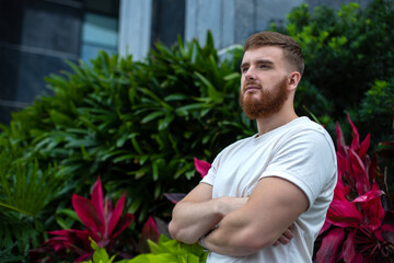 Portrait of happy young bearded man with beard breathing deep, inhale fresh air on natural background, green wall with leaves, flower in tropical country in garden. Eco, ecological concept. 