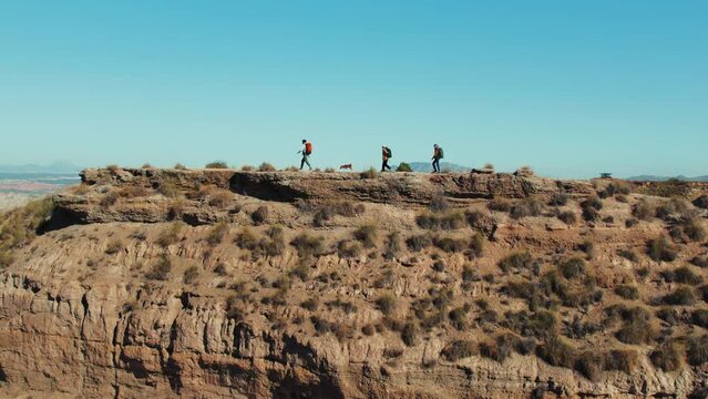 At the summer heat, a group of tourists with dog hikes up a desert hill, guided by their explorer. The scenic view from the top offers a peaceful respite, inspiring wanderlust and adventure.