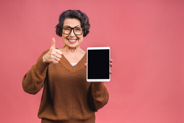 Portrait of senior aged mature woman with tablet computer, grandmother isolated on pink background....