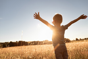 It's a beautiful life! Child standing with arms up facing the sunrise having feelings of freedom,...