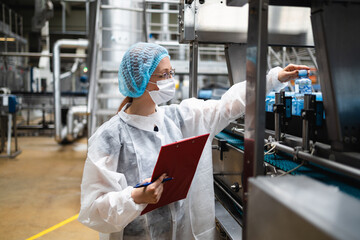 Female worker in protective workwear working in medical supplies research and production factory. She is standing on control bridge and watching at production line. Inspection quality control.