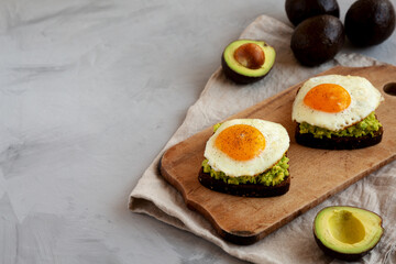 Homemade Avocado Toast with Eggs on a rustic wooden board, side view. Copy space.
