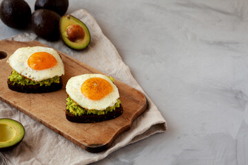 Homemade Avocado Toast with Eggs on a rustic wooden board, side view. Copy space.