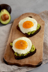 Homemade Avocado Toast with Eggs on a rustic wooden board, side view.