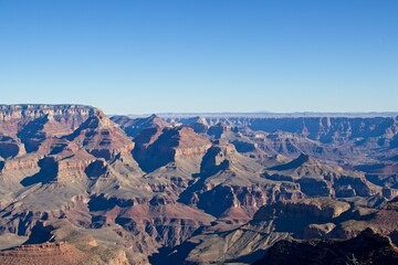 Bright desert sunlight shines down on the Grand Canyon, casting shadows on every crease and layer of the eroded canyon carved over many years by the Colorado River thousands of feet below