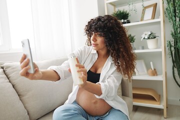 Pregnant woman smile blogger showing baby feeding bottle filming herself on phone, video chat...