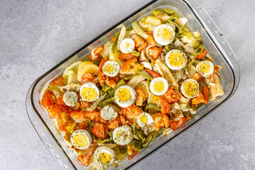Gomes de sa codfish roasted in olive oil with tomatoes, peppers, onions, boiled eggs and oregano. In a rectangular glass baking dish.