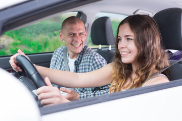 Young attractive girl driving car with man in passenger seat during trip, side view